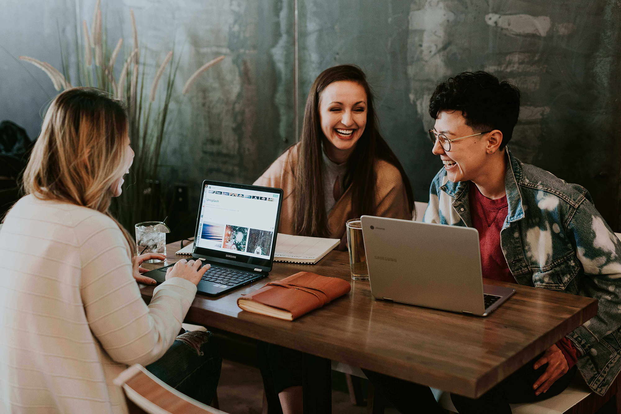 Drie lachende vrouwen achter hun laptops aan een tafel
